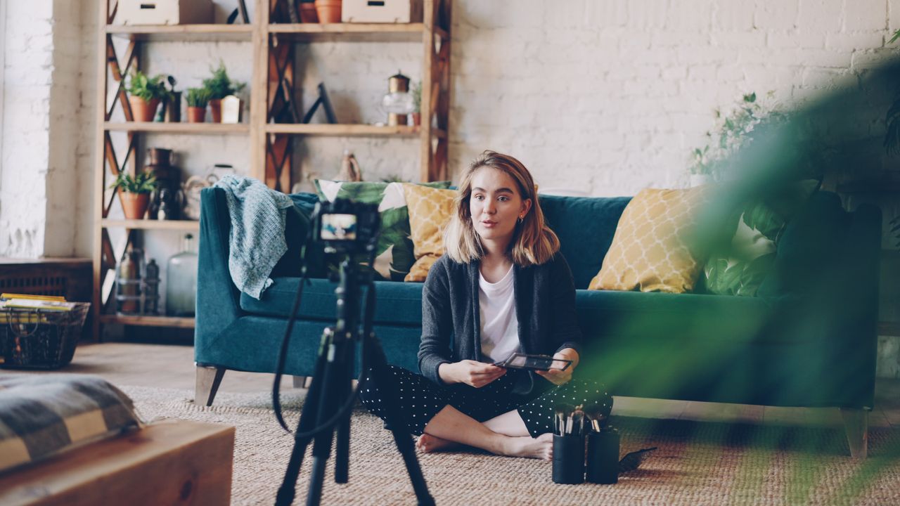 The Art of Drawing Readers In: Your attractive post title goes here Woman filming vlog at home with camera setup, surrounded by plants and cozy decor.