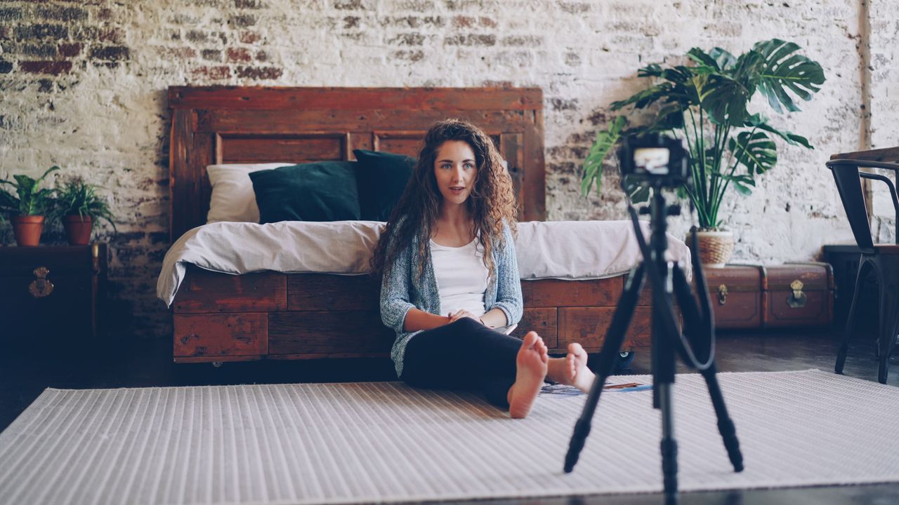 Crafting Captivating Headlines: Your awesome post title goes here Woman seated in bedroom with camera, creating content in relaxed environment.