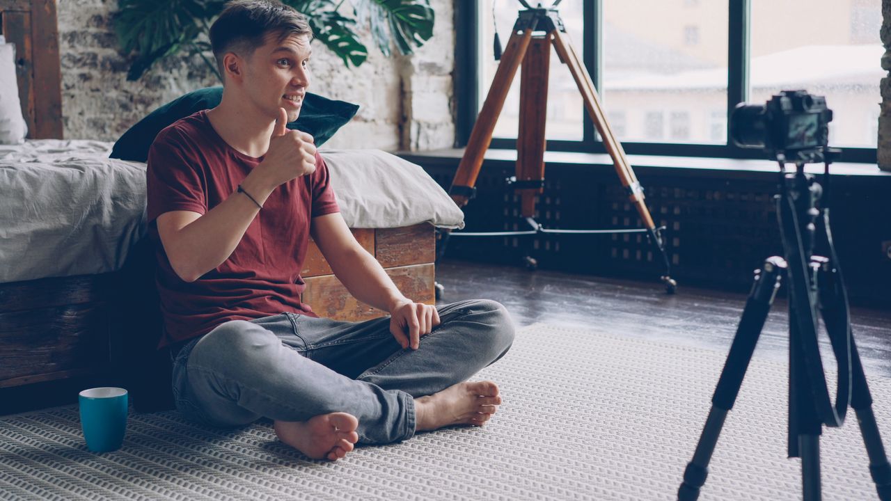 Mastering the First Impression: Your intriguing post title goes here Young man sitting on the floor filming a video at home, surrounded by tripod and camera.
