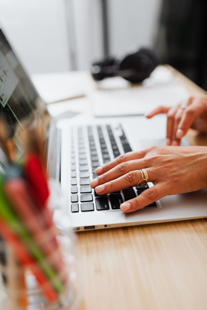 About Hands with rings typing on a laptop keyboard in a bright workspace.